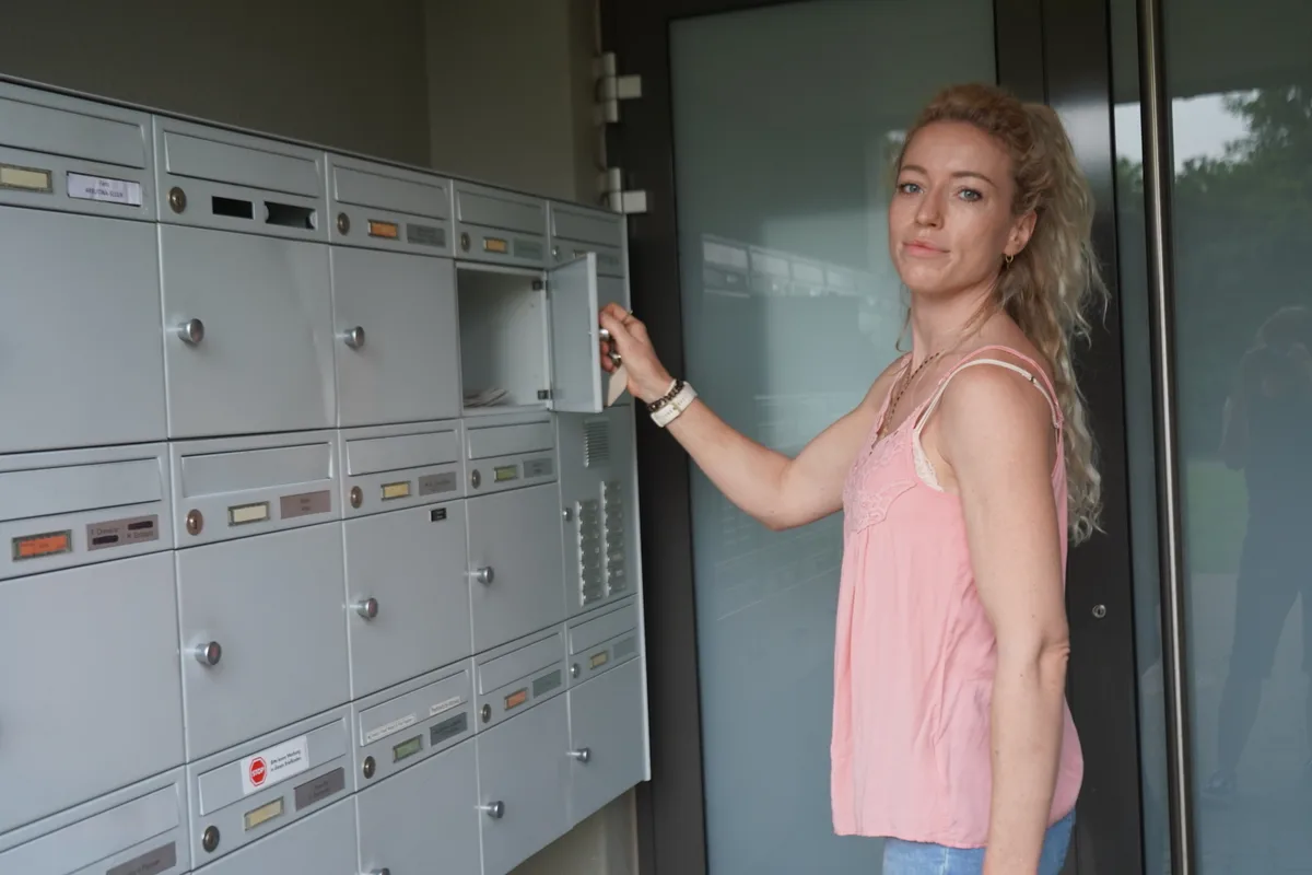 Man sieht eine Frau, die ihren Briefkasten öffnet.